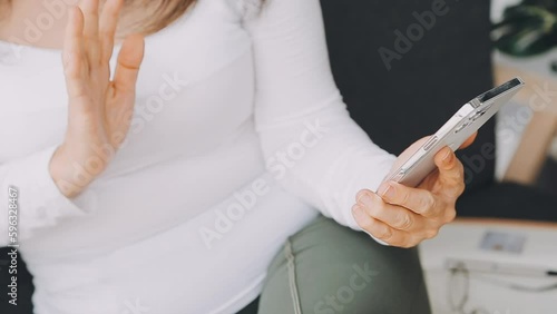 From above of positive adult female in casual outfit with headphones and tablet sitting on sofa with pillows in light studio photo