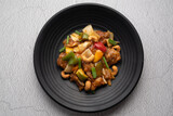 Stir fried chicken with cashew nuts in black dish on concrete table.