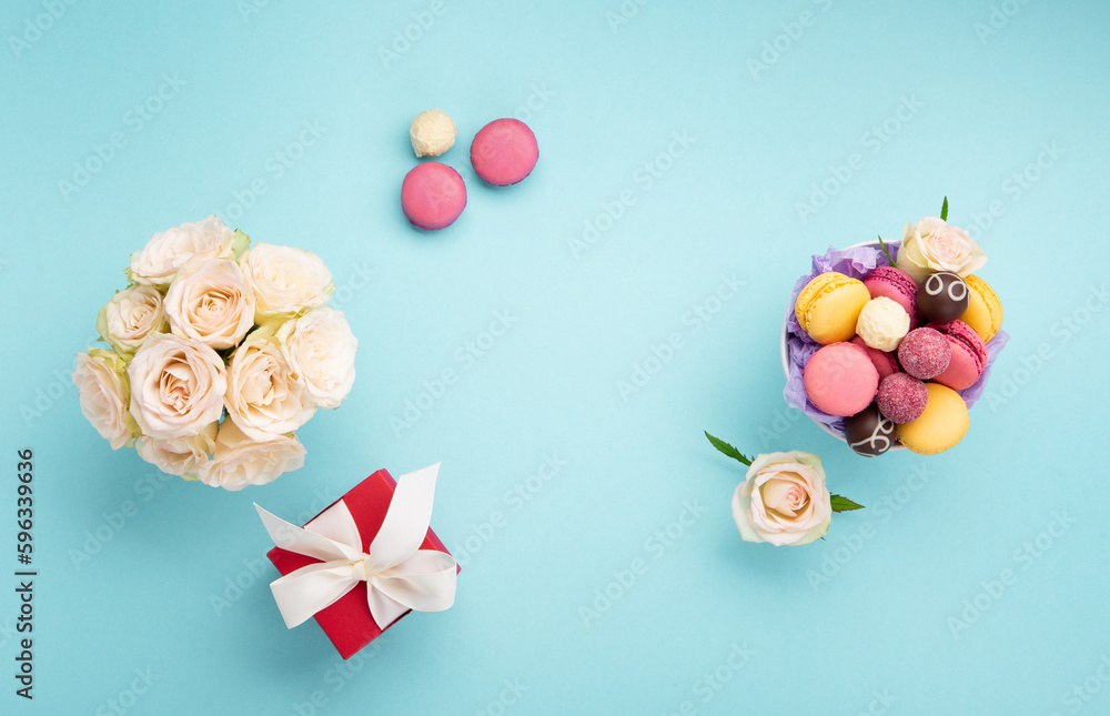 Macaroons, Gift Box, Rose Flowers and Chocolate Candies on Blue Background. Spring Presents Concept