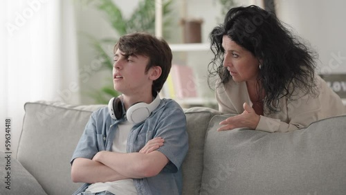 Woman giving advice to son and the teenager boy ignoring her putting on the headphones and starting to play video game