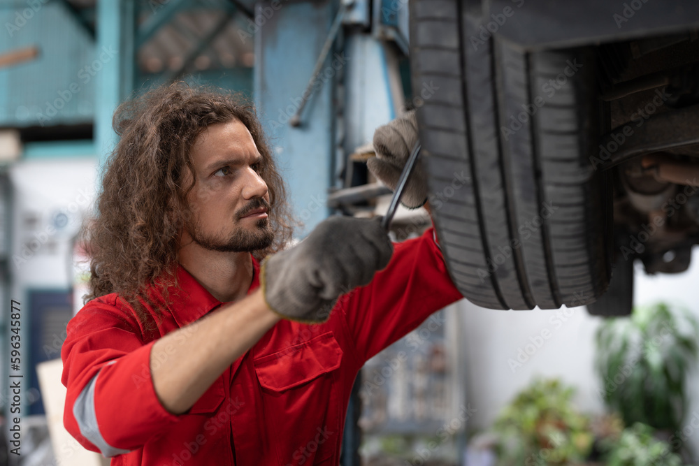 Car mechanic man in red uniform using spanner to changing car wheel at