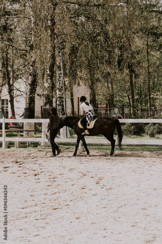 A woman instructor teaching girl how to ride a horse. Female rider practicing on a horseback learning equestrian sport. Active lifestyle and leisure activity concep A woman instructor teaching girl how to ride a horse. Female rider practicing on a horseback learning equestrian sport. Active lifestyle and leisure activity concep