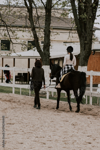 A woman instructor teaching girl how to ride a horse. Female rider practicing on a horseback learning equestrian sport. Active lifestyle and leisure activity concep