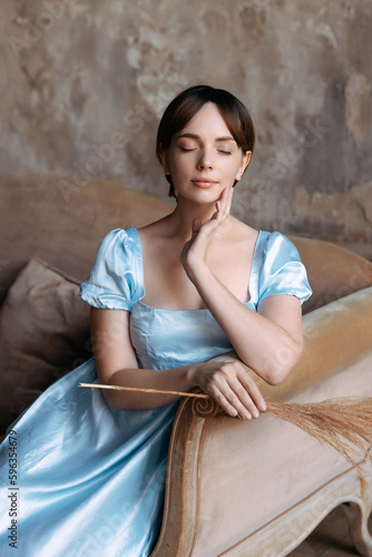 A young beautiful girl in a blue dress of the Regency era sits on a sofa in an old estate. Classic artistic image of Russian literature of the 19th century, outdated.