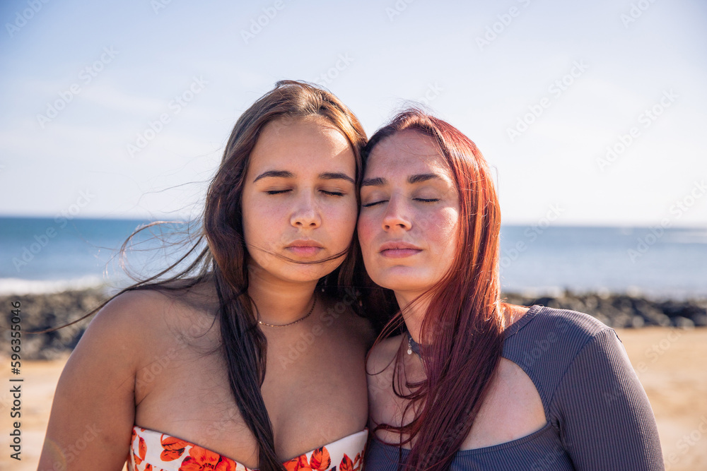 Two sisters pose with faces close and eyes closed at the beach, love between sisters Two sisters pose with faces close and eyes closed at the beach, love between sisters