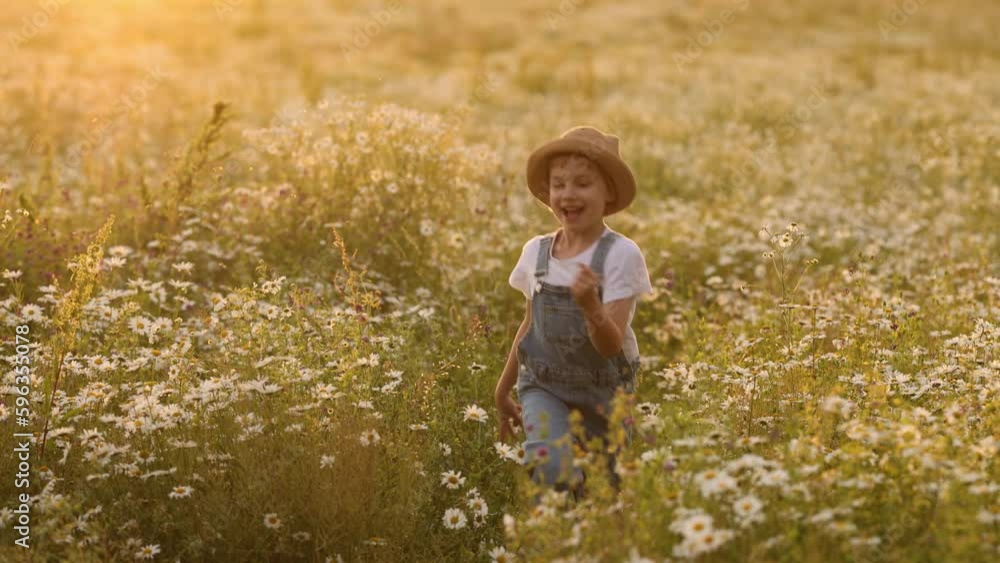 A beautiful smiling girl in a straw hat and denim overalls runs through a field of daisies. The concept of a weekend in nature or a vacation with a grandmother in nature. A beautiful smiling girl in a straw hat and denim overalls runs through a field of daisies. The concept of a weekend in nature or a vacation with a grandmother in nature.