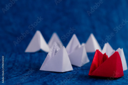 Low angle front close up shot of a red paper boat with many white boats in blue ocean. © winistudios