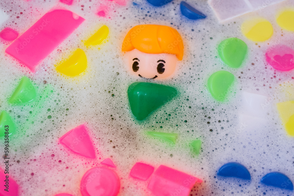 Washing of children toys, plastic building blocks with figurines. A smiling little fellow and colorful cubes float in the foaming water