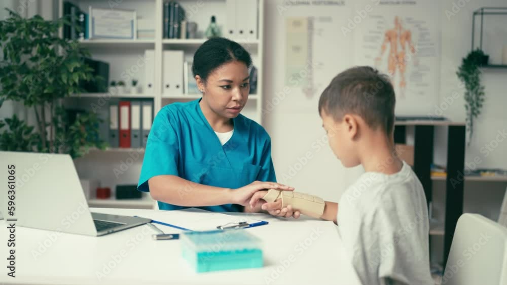 Female doctor putting immobilizer on boy's injured hand, trauma treatment Female doctor putting immobilizer on boy's injured hand, trauma treatment