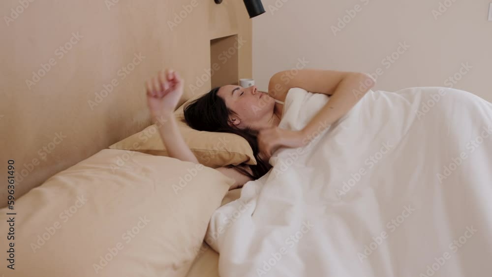 Side view of Young brunette woman sleeps peacefully on bed, wakes up, stretches, puts duvet on head and goes back to sleep in the morning. Doesn't want to wake up. Horizontal, hd video 4k resolution. Side view of Young brunette woman sleeps peacefully on bed, wakes up, stretches, puts duvet on head and goes back to sleep in the morning. Doesn't want to wake up. Horizontal, hd video 4k resolution.