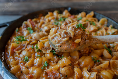 Ground beef with cream, cheese and pasta shells in a cast  iron pan with wooden spoon