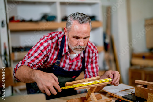 Professional senior carpenter man use tape measure to work with timber in woodwork factory workplace with happiness.