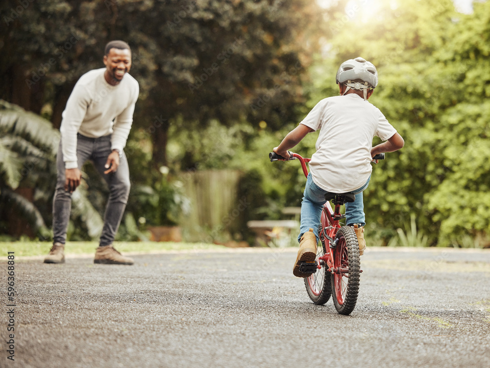 Come on now. Shot of an adorable boy learning to ride a bicycle with his father outdoors.