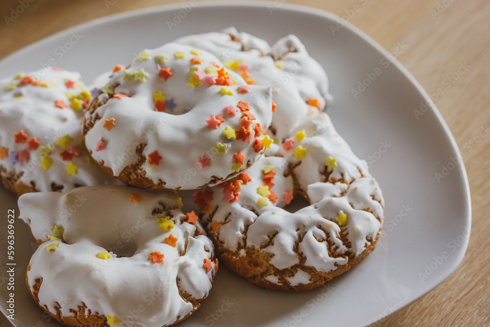 A plate of sweets with white icing, yellow red sprinkles Homemade Doughnuts, rosquillas, traditional anise donuts from Spain typically eaten in Easter, on rustic wooden table. Mediterranean sweet food A plate of sweets with white icing, yellow red sprinkles Homemade Doughnuts, rosquillas, traditional anise donuts from Spain typically eaten in Easter, on rustic wooden table. Mediterranean sweet food