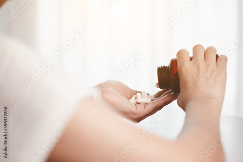 Asian woman's hand pouring medicines from a brown bottle