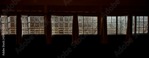 Interior de casa antiga de madeira com diversas janelas quadradas com cortina. Ambiente escuro e vazio sem pessoas