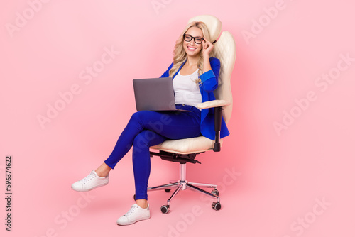 Full length photo of charming professional lady sit office chair use technology laptop wear suit specs isolated pink color background