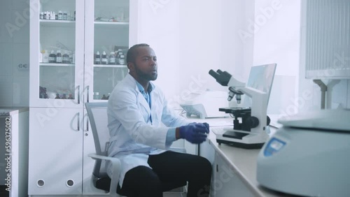 Wallpaper Mural Shot of African American lab worker in white labcoat looking through microscope while conducting scientific experiment indoors. Medical development laboratory. Male scientist working in advanced Torontodigital.ca