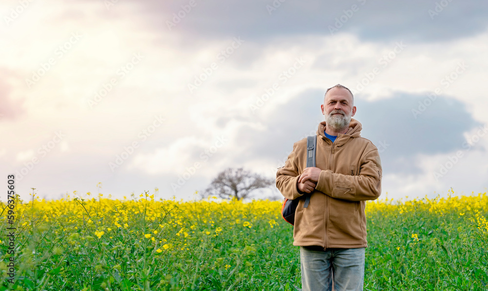 Bearded happy pensioner with a backpack in the rapeseed field.  Travel  Lifestyle concept