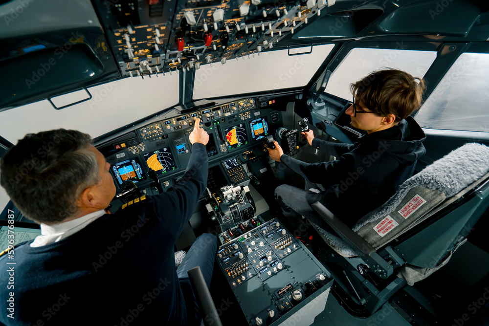 An experienced pilot instructs a young student before a training flight in the cockpit of an aero simulator - obrazy, fototapety, plakaty 