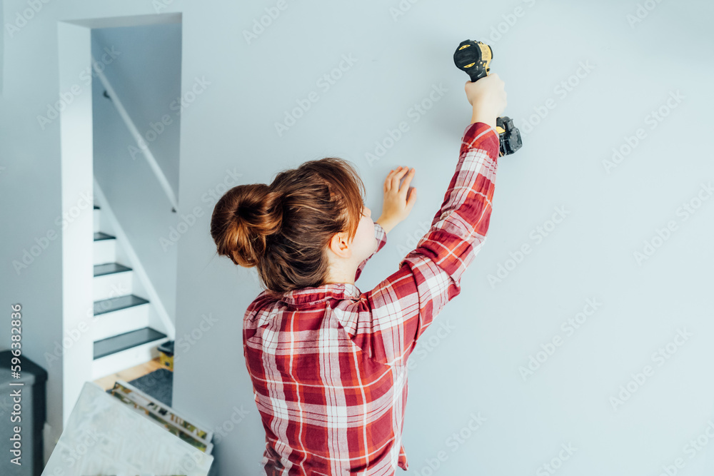 Back view young woman screwing screw into wall with electrical