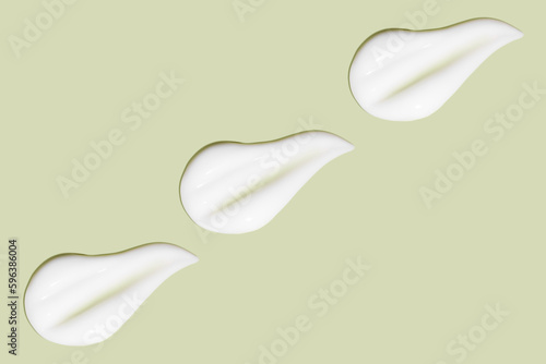 Lots of smears of cosmetic cream. Light  smooth surface.  In a row. At an angle. Top view. Texture of flowing cream. Liquid creamy strokes. On green background. Cosmetic background  banner.