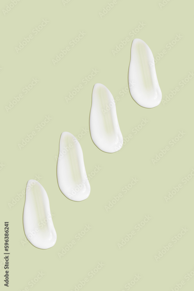 Lots of smears of cosmetic cream. Light, smooth surface. In a row. At an angle. Top view. Texture of flowing cream. Liquid creamy strokes. On green background. Cosmetic background, banner. Lots of smears of cosmetic cream. Light, smooth surface. In a row. At an angle. Top view. Texture of flowing cream. Liquid creamy strokes. On green background. Cosmetic background, banner.