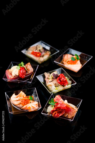 Restaurant menu of appetizers of scorched salmon, tuna, white fish with red caviar, sun-dried tomatoes, spices and microgreens.