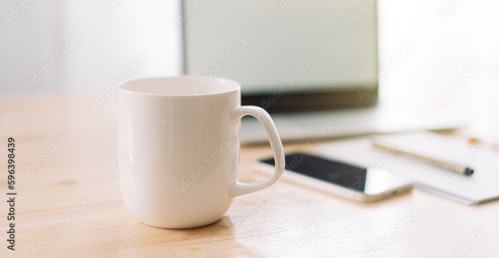 Fototapeta premium White mug without inscriptions opposite laptop and notepad with pen on wooden table.