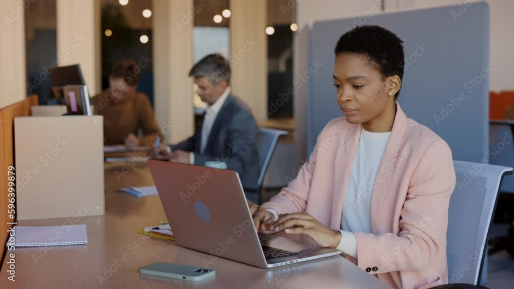 African American businesswoman sitting at desk and typing on laptop computer in contemporary corporation office. She crossed arms and smile while finished her work. Business technologies concept. African American businesswoman sitting at desk and typing on laptop computer in contemporary corporation office. She crossed arms and smile while finished her work. Business technologies concept.