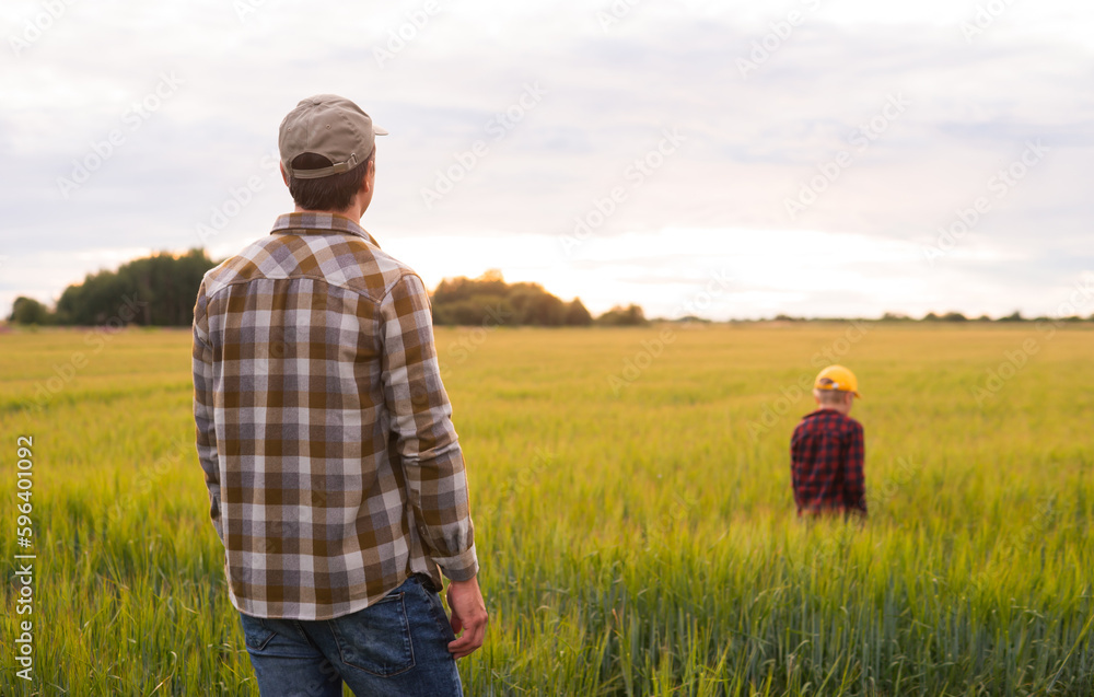 Farmer and his son in front of a sunset agricultural landscape. Man and a boy in a countryside field. Fatherhood, country life, farming and country lifestyle concept.
