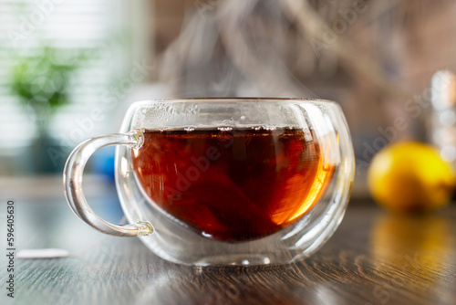 A hot cup of freshly brewed black tea with steam on wooden table