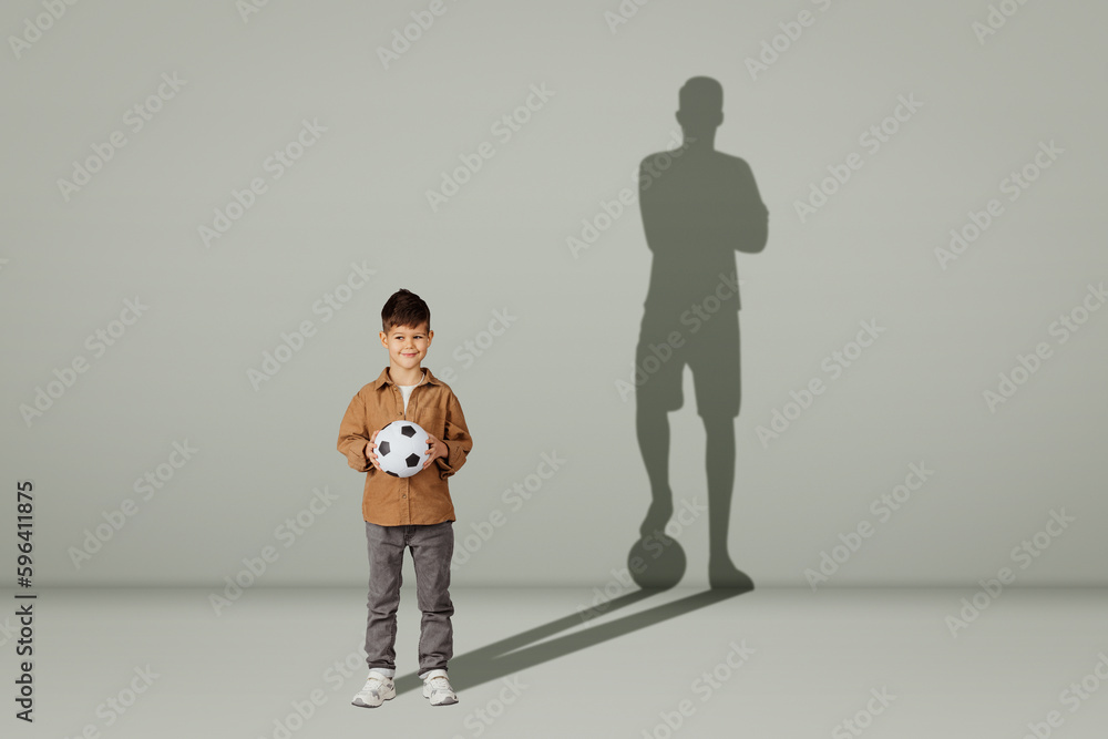 Positive caucasian 6 years old little child in casual with soccer ball and shadow of young soccer player Positive caucasian 6 years old little child in casual with soccer ball and shadow of young soccer player