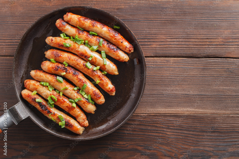Delicious sausages cooked in a frying pan on a wooden table. copy space. Delicious sausages cooked in a frying pan on a wooden table. copy space.