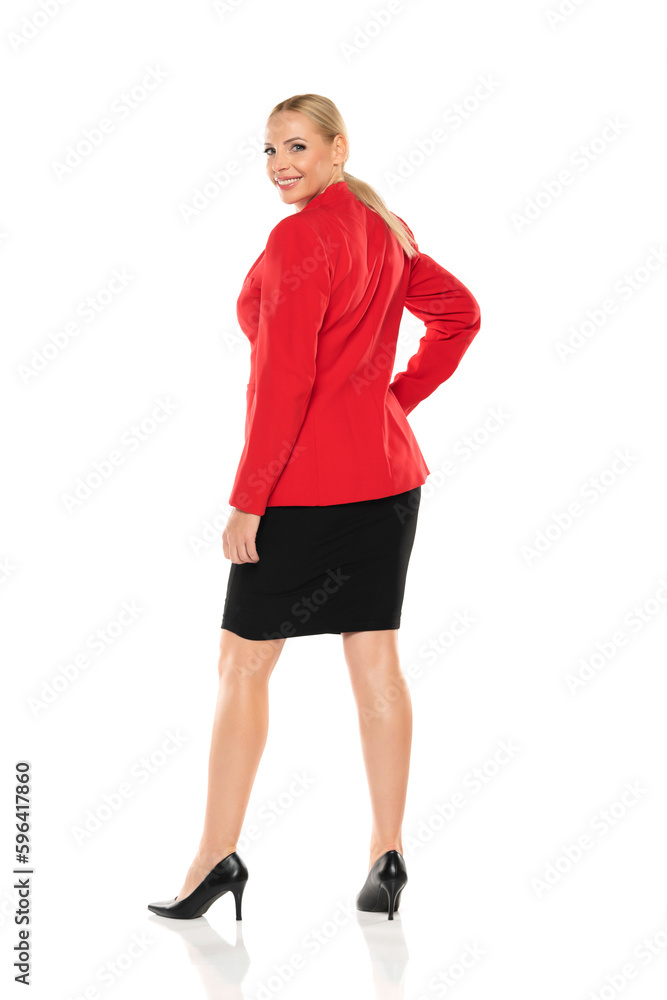 Middle aged senior smiling business woman in red jacket and black skirt posing on white background. Back, rear view. Middle aged senior smiling business woman in red jacket and black skirt posing on white background. Back, rear view.