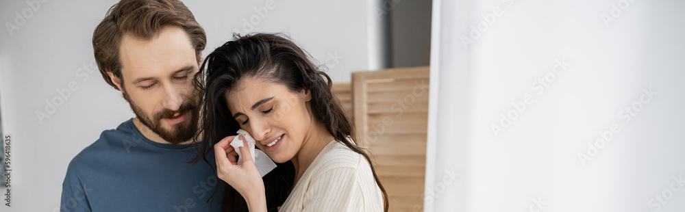 Displeased woman holding napkin and crying near bearded boyfriend at home, banner. Displeased woman holding napkin and crying near bearded boyfriend at home, banner.