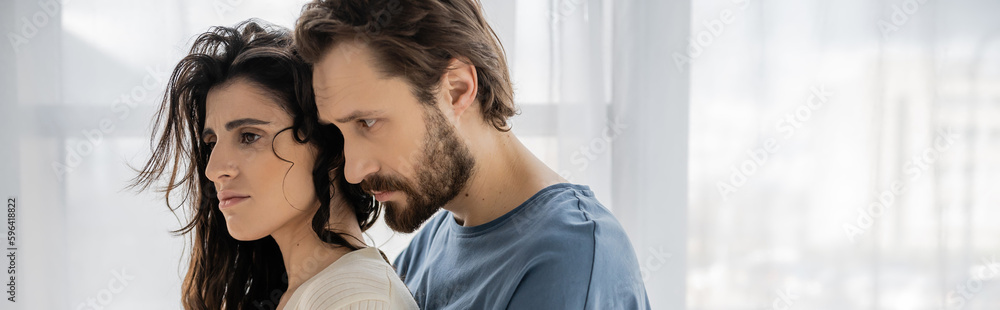 Bearded man looking at upset brunette girlfriend at home, banner. Bearded man looking at upset brunette girlfriend at home, banner.