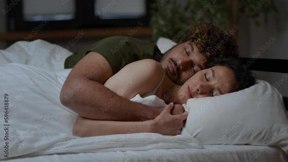 Young middle eastern couple in love sleeping in bed and hugging, man embracing his wife late in night, tracking shot