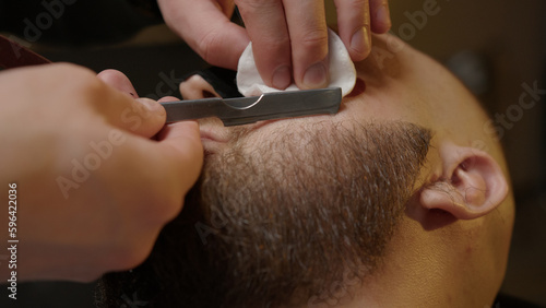 Barber corrects upper line of beard. Hairdresser shaves with dangerous razor