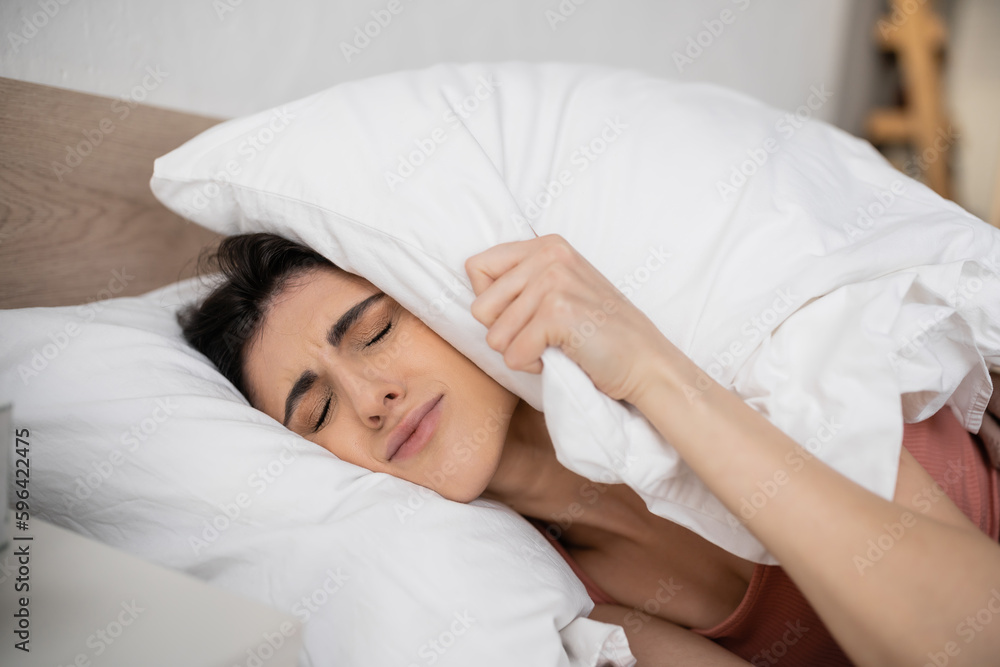 Upset brunette woman putting pillow on head on bedroom in morning. Upset brunette woman putting pillow on head on bedroom in morning.