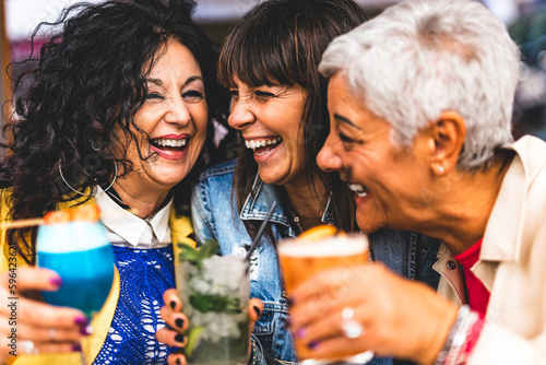 Group of three mature women drinking cocktails outdoors at bar restaurant-Happy senior friends enjoying happy hour holding fancy drink at city pub - Life Style and Fun concept with older female