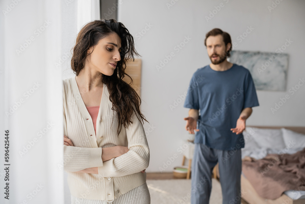 Upset woman crossing arms while blurred boyfriend quarrelling at home. Upset woman crossing arms while blurred boyfriend quarrelling at home.