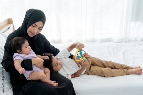 Muslim family, an Asian mother holding baby newborn daughter and hugging son is half-Thai-Nigerian, lying on his mother's lap. to  relationship in Muslim family and baby newborn concept. photo