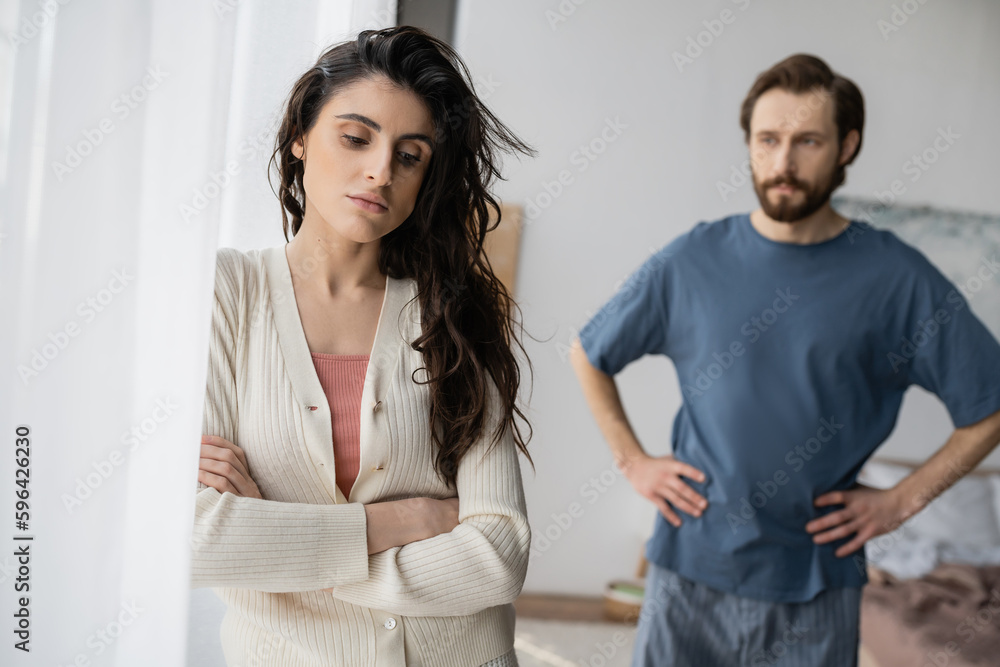 Sad woman standing near blurred boyfriend during relationship difficulties at home. Sad woman standing near blurred boyfriend during relationship difficulties at home.