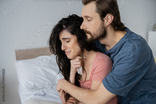 Konstfotografi Bearded man hugging dissatisfied girlfriend with napkin in bedroom