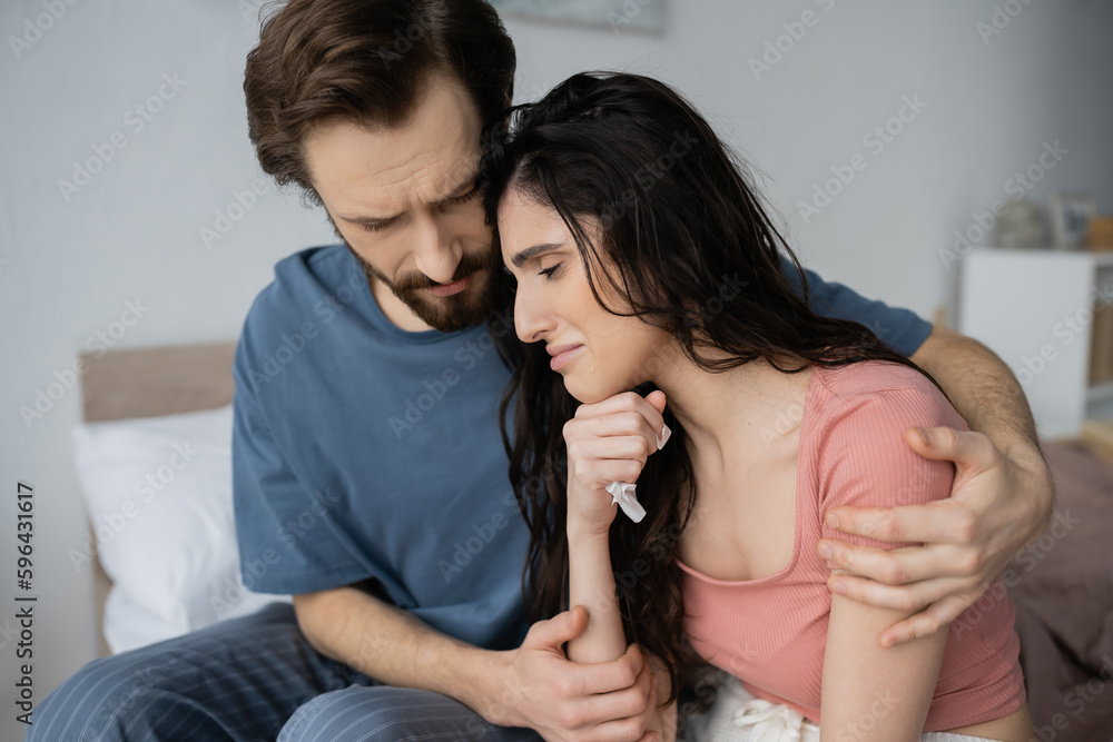 Empathetic man in pajama calming crying girlfriend with napkin in bedroom. Empathetic man in pajama calming crying girlfriend with napkin in bedroom.