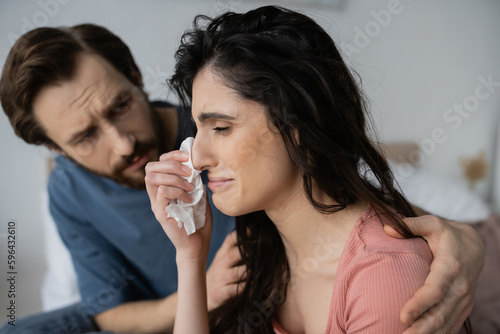 Displeased woman crying near caring blurred boyfriend at home.