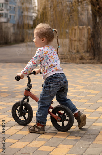 Fototapeta Naklejka Na Ścianę i Meble -  cheerful little child girl from behind riding on bike in the city park outdoors