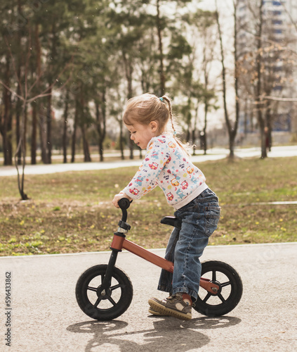 little child girl sitting on a bike in the city park in sunny day outdoors © Оксана Рязанова
