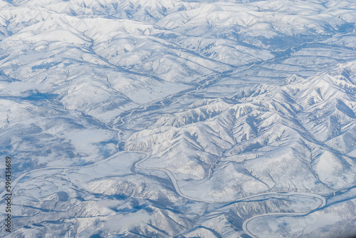 Aerial view of a winding river among high hills and mountains in the tundra. Siberia, Far East of Russia. Snow-covered tundra in the Arctic.